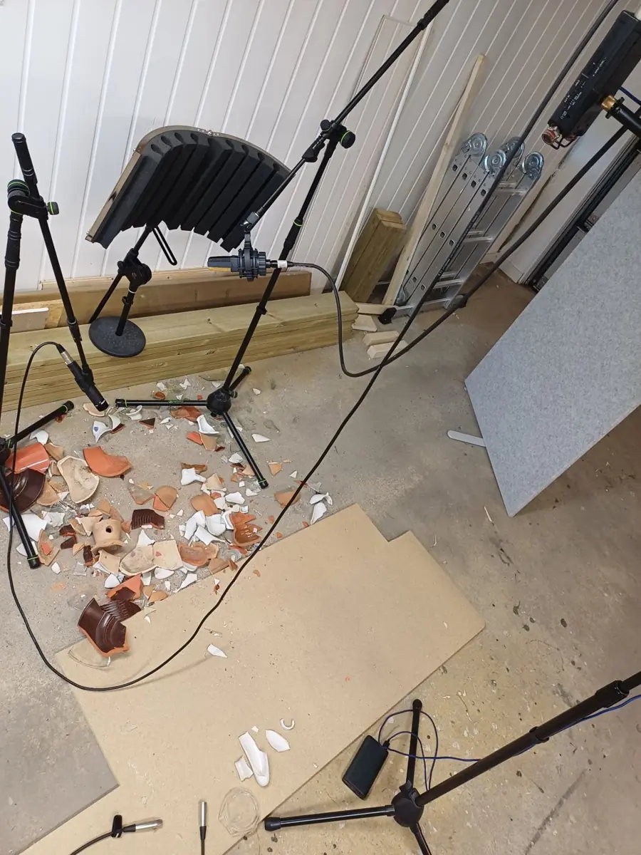 Broken plates and pottery on a concrete floor surrounded by three microphones